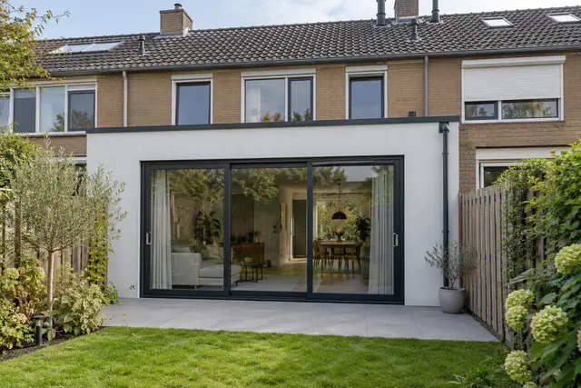 uitbouw in wit stucwerk met een zwarte schuifpui over de volle breedte, aan de achterkant van een rijwoning